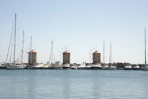 Three beautiful ancient stone Windmills in the Mandraki port with some cruise boats at Rhodes, Greece. Behind on the left you can see the cassel of the old medieval town.