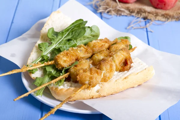 Lezzetli altın derin kızarmış pirzola midye şişleri yoğurt sos tartar ile hizmet veren sandviç, domates, dilimlenmiş beyaz soğan, maydanoz ve yeşil roka salatası mavi rustik masa arka plan üzerinde. Midye tava ekmek.