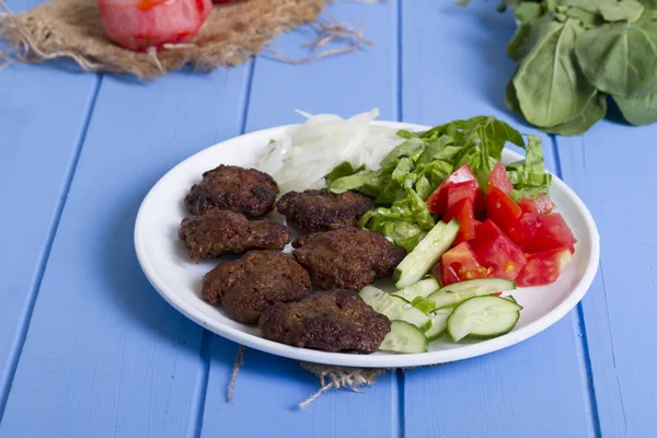 Izgara sığır eti köfte porsiyon dilimlenmiş salatalık, beyaz soğan, küp daire plakalı domates ve marul salatası mavi rustik ahşap masanın üstüne kesmek. Ekmek kırıntıları, tereyağı ve baharat gibi maddeler.