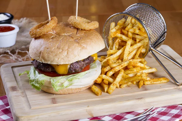 Ev yapımı hamburger marul, soğan, mantar, domates dilimleri, turşu, pastırma ve kaşar peynir porsiyon kızarmış baharatlı patates kızartması ile ahşap masa arka plan üzerinde.