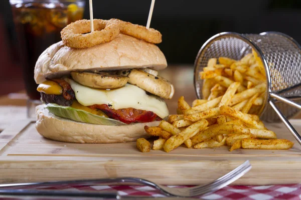 Ev yapımı hamburger marul, soğan, mantar, domates dilimleri, turşu, pastırma ve kaşar peynir porsiyon kızarmış baharatlı patates kızartması ile ahşap masa arka plan üzerinde.