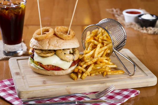 Ev yapımı hamburger marul, soğan, mantar, domates dilimleri, turşu, pastırma ve kaşar peynir porsiyon kızarmış baharatlı patates kızartması ile ahşap masa arka plan üzerinde.