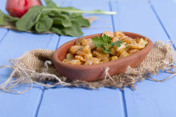 Lezzetli küçük kırmızı karides tereyağı ile baharat baharat haşlanmış. Geleneksel Yunan çanak çömlek içinde hizmet veren karides güveç. Üstten görünüm mavi rustik arka plan. En ortak gıda alerjenleri arasında diğer kabuklu deniz ürünleri.