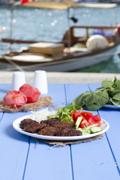 Izgara sığır eti köfte porsiyon dilimlenmiş salatalık, beyaz soğan, küp daire plakalı domates ve marul salatası mavi rustik ahşap masanın üstüne kesmek. Ekmek kırıntıları, tereyağı ve baharat gibi maddeler.