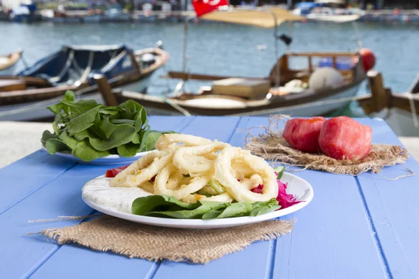 Lezzetli derin kızarmış kalamar garson beyaz daire plaka, kırmızı lahana, tartar, halka dilimlenmiş soğan ve yeşil roka salatası rustik mavi ahşap arka plan üzerinde. Kalamar çok mutfaklarının yemek. Üstten görünüm.