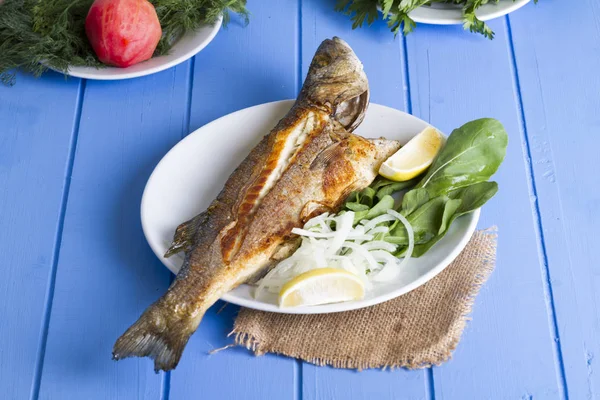 Yeşil ve mavi ahşap masa, deniz ürünleri kavramı üzerinde limon ile ızgara levrek balık