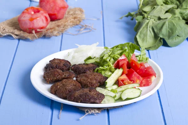 Izgara sığır eti köfte porsiyon dilimlenmiş salatalık, beyaz soğan, küp daire plakalı domates ve marul salatası mavi rustik ahşap masanın üstüne kesmek. Ekmek kırıntıları, tereyağı ve baharat gibi maddeler.