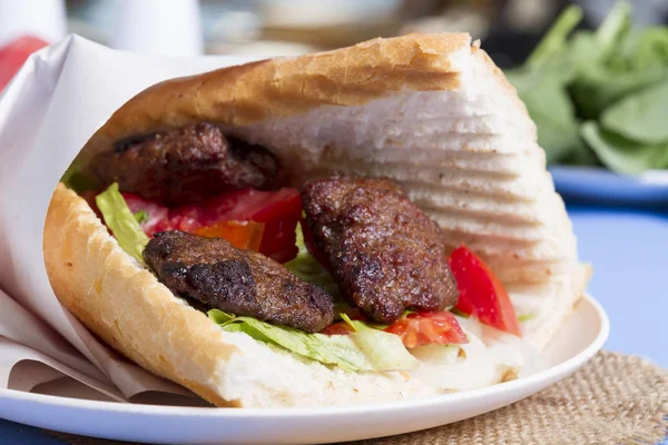Delicious Turkish Meatballs Sandwich, Kofte Ekmek. Ingredients with bread crumbs, butter, sliced onion, cucumber, tomato, lettuce salad, pickles and seasoning spices. Hamburger serving on blue table.