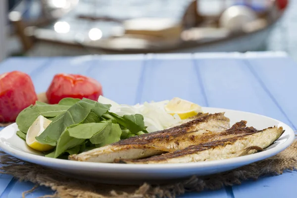 Lezzetli ızgara fileto levrek porsiyon dilimlenmiş soğan, domates, yeşil roka salatası ve sulu limon rustik mavi ahşap masa arka plan üzerinde oval beyaz plakalı füme. Alan, kopyalama kimse.