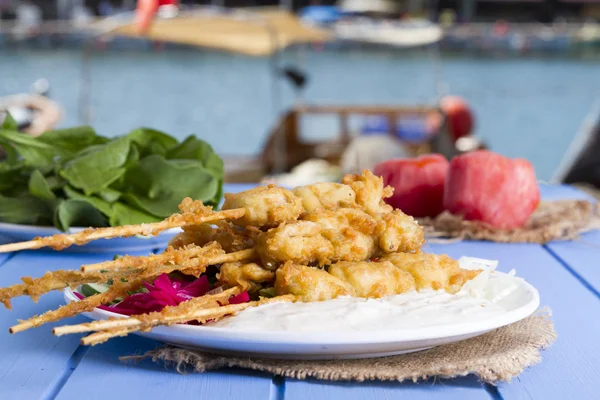 Lezzetli altın derin kızarmış pirzola midye yoğurt sos tartar ile hizmet veren şişleri, domates, dilimlenmiş beyaz soğan, maydanoz ve yeşil roka salatası mavi rustik masa arka plan üzerinde. Midye tava.