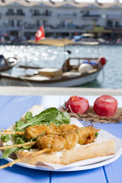 Lezzetli altın derin kızarmış pirzola midye şişleri yoğurt sos tartar ile hizmet veren sandviç, domates, dilimlenmiş beyaz soğan, maydanoz ve yeşil roka salatası mavi rustik masa arka plan üzerinde. Midye tava ekmek.