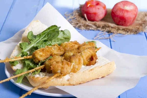 Lezzetli altın derin kızarmış pirzola midye şişleri yoğurt sos tartar ile hizmet veren sandviç, domates, dilimlenmiş beyaz soğan, maydanoz ve yeşil roka salatası mavi rustik masa arka plan üzerinde. Midye tava ekmek.