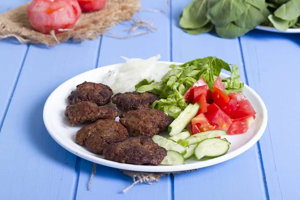 Izgara sığır eti köfte porsiyon dilimlenmiş salatalık, beyaz soğan, küp daire plakalı domates ve marul salatası mavi rustik ahşap masanın üstüne kesmek. Ekmek kırıntıları, tereyağı ve baharat gibi maddeler.