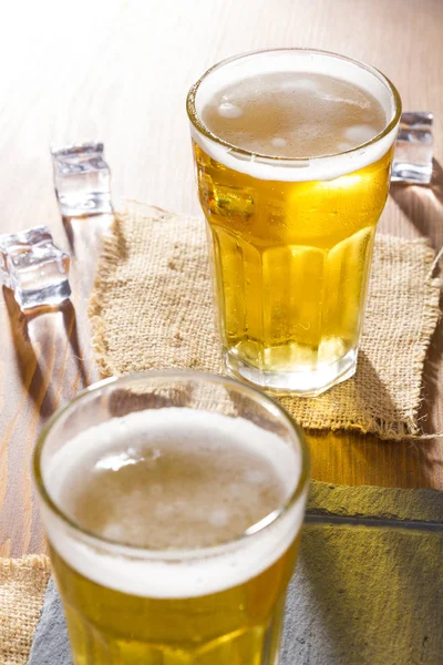 Two Cold Golden Chilled Glasses of Draft Beer Served on wood bar counter.