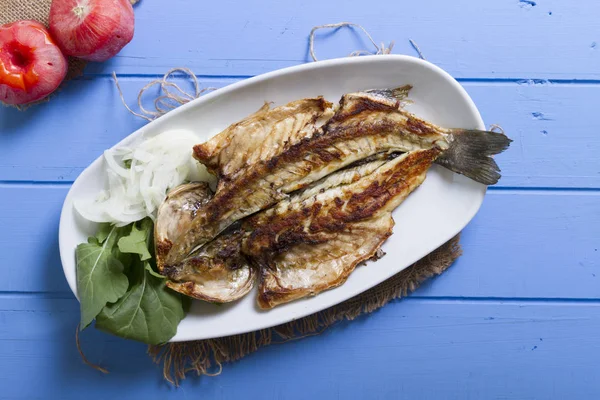 Lezzetli ızgara fileto levrek porsiyon dilimlenmiş soğan, domates, yeşil roka salatası ve sulu limon rustik mavi ahşap masa arka plan üzerinde oval beyaz plakalı füme. Alan, kopyalama kimse.