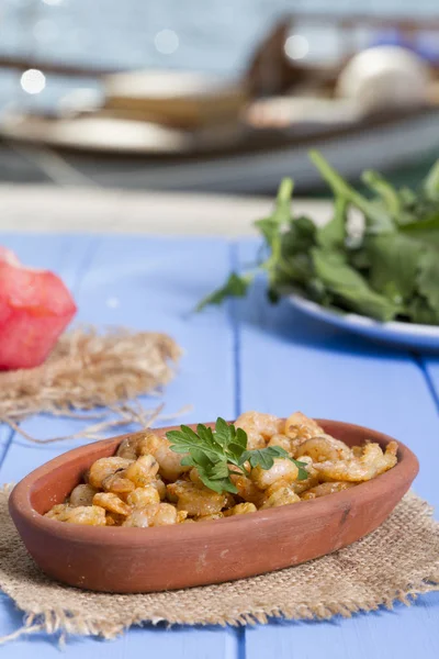 Lezzetli küçük kırmızı karides tereyağı ile baharat baharat haşlanmış. Geleneksel Yunan çanak çömlek içinde hizmet veren karides güveç. Üstten görünüm mavi rustik arka plan. En ortak gıda alerjenleri arasında diğer kabuklu deniz ürünleri.