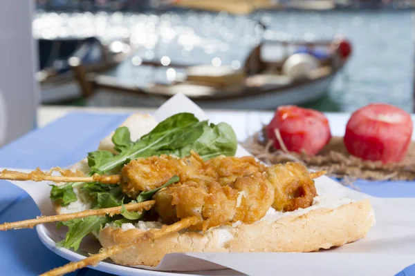 Lezzetli altın derin kızarmış pirzola midye şişleri yoğurt sos tartar ile hizmet veren sandviç, domates, dilimlenmiş beyaz soğan, maydanoz ve yeşil roka salatası mavi rustik masa arka plan üzerinde. Midye tava ekmek.