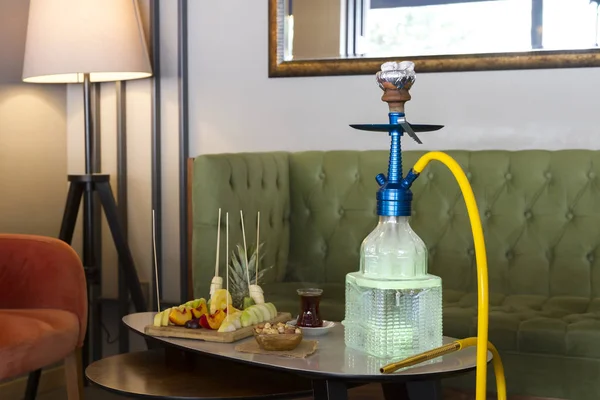 Traditional Arabic and Turkish shisha, hookah or Water pipe serving with fresh fruits, hot black tea and nuts on table, modern cafe lounge design. Led light in water.