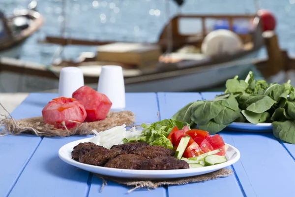 Izgara sığır eti köfte porsiyon dilimlenmiş salatalık, beyaz soğan, küp daire plakalı domates ve marul salatası mavi rustik ahşap masanın üstüne kesmek. Ekmek kırıntıları, tereyağı ve baharat gibi maddeler.