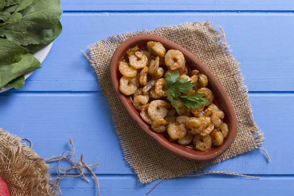 Lezzetli küçük kırmızı karides tereyağı ile baharat baharat haşlanmış. Geleneksel Yunan çanak çömlek içinde hizmet veren karides güveç. Üstten görünüm mavi rustik arka plan. En ortak gıda alerjenleri arasında diğer kabuklu deniz ürünleri.