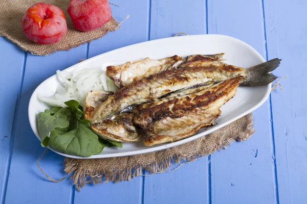 Lezzetli ızgara fileto levrek porsiyon dilimlenmiş soğan, domates, yeşil roka salatası ve sulu limon rustik mavi ahşap masa arka plan üzerinde oval beyaz plakalı füme. Alan, kopyalama kimse.