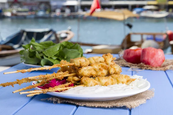 Lezzetli altın derin kızarmış pirzola midye yoğurt sos tartar ile hizmet veren şişleri, domates, dilimlenmiş beyaz soğan, maydanoz ve yeşil roka salatası mavi rustik masa arka plan üzerinde. Midye tava.