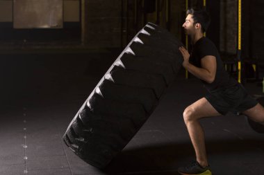 Adam lastiği döndürür, çapraz formda fonksiyonel spor. Spor salonunda spor eğitimi alan genç bir adam..