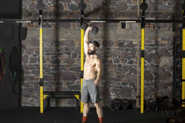 Genç sakallı ve halter pratik gömleksiz atlet spor salonunda kaçırır. Kopyalama alanı alanı konseptiyle karanlık fotoğraf. 