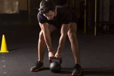 Kettlebell pratik genç atlet spor salonunda sallanır. Karanlık fotoğraf kavramı kopya alanı ile.