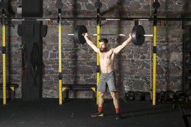 Ağır bir halter salonunda ile eğitim genç sakallı ve gömleksiz atlet. Kopyalama alanı alanı konseptiyle karanlık fotoğraf.