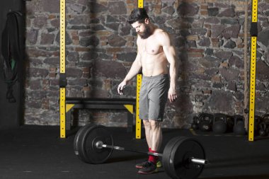 Ağır bir halter salonunda ile eğitim genç sakallı ve gömleksiz atlet. Kopyalama alanı alanı konseptiyle karanlık fotoğraf.