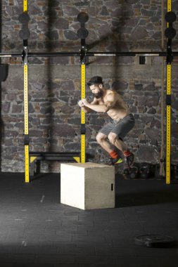 Bir çapraz eğitim spor salonunda bir kutu üzerine atlama yakışıklı güçlü gömleksiz adam. Karanlık fotoğraf konsepti ile kopyalama alanı metin alanı.