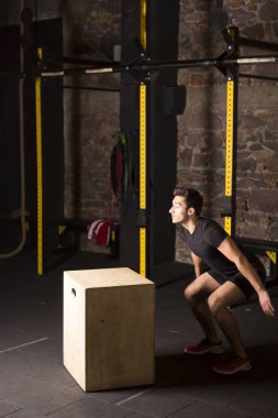 Yaklaşık bir çapraz eğitim spor salonunda bir kutu üzerine atlamak için yakışıklı güçlü İspanyol adam. Karanlık fotoğraf konsepti ile kopyalama alanı metin alanı.