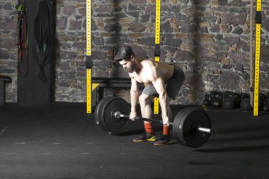 Ağır bir halter salonunda ile eğitim genç sakallı ve gömleksiz atlet. Kopyalama alanı alanı konseptiyle karanlık fotoğraf.