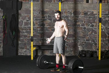 Ağır bir halter salonunda ile eğitim genç sakallı ve gömleksiz atlet. Kopyalama alanı alanı konseptiyle karanlık fotoğraf.