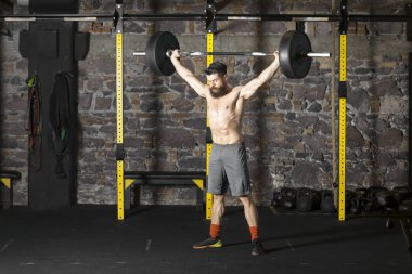 Ağır bir halter salonunda ile eğitim genç sakallı ve gömleksiz atlet. Kopyalama alanı alanı konseptiyle karanlık fotoğraf.