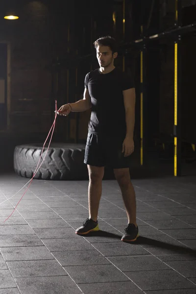 Young athlete doing jump rope exercises at the gym. Dark photography concept with copy space text area.