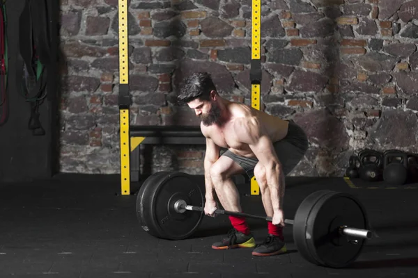 Ağır bir halter salonunda ile eğitim genç sakallı ve gömleksiz atlet. Kopyalama alanı alanı konseptiyle karanlık fotoğraf.