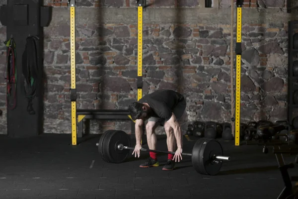 Young beard athlete training with a heavy barbell at the gym. Dark photography concept with copy space area.