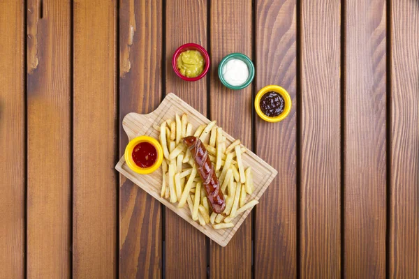 Top view of Grilled pork frankfurter sausage with french fries, chips and dip sauces.