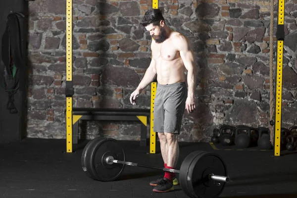 Ağır bir halter salonunda ile eğitim genç sakallı ve gömleksiz atlet. Kopyalama alanı alanı konseptiyle karanlık fotoğraf.