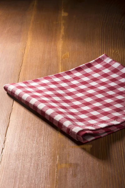 Red and white square scotch pattern napkin on wood table background with dramatic dark light.