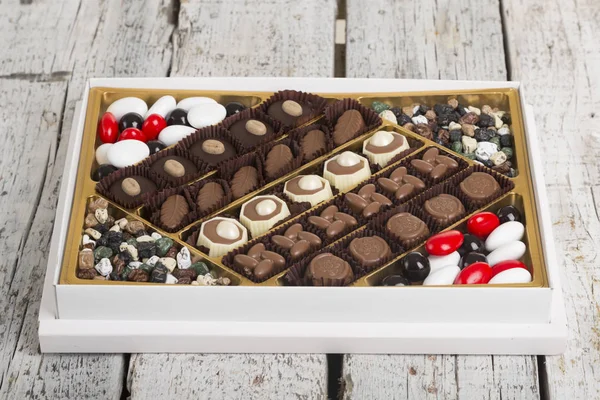 Luxury Box of Assorted handmade chocolate truffles on white wooden rustic background. Chocolates in different shapes and colors in paper box. Above angle view. Copy space for text area.