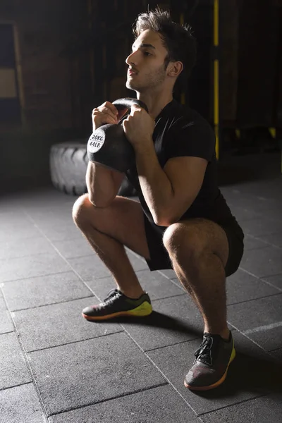 Genç Erkek atlet kadehi pratik Ireland ile spor salonunda squats. Karanlık fotoğraf konsepti ile kopyalama alanı metin alanı.