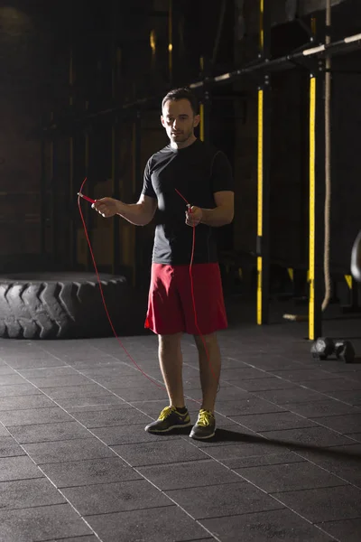 Young athlete doing jump rope exercises at the gym. Dark photography concept with copy space text area.