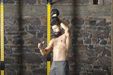 Genç sakallı ve halter pratik gömleksiz atlet spor salonunda kaçırır. Kopyalama alanı alanı konseptiyle karanlık fotoğraf. 