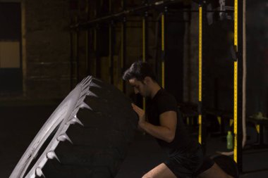 Adam lastiği döndürür, çapraz formda fonksiyonel spor. Spor salonunda spor eğitimi alan genç bir adam..