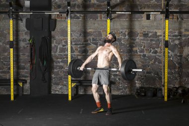 Ağır bir halter salonunda ile eğitim genç sakallı ve gömleksiz atlet. Kopyalama alanı alanı konseptiyle karanlık fotoğraf.