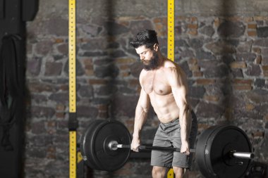 Ağır bir halter salonunda ile eğitim genç sakallı ve gömleksiz atlet. Kopyalama alanı alanı konseptiyle karanlık fotoğraf.