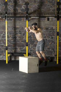 Bir çapraz eğitim spor salonunda bir kutu üzerine atlama yakışıklı güçlü gömleksiz adam. Karanlık fotoğraf konsepti ile kopyalama alanı metin alanı.